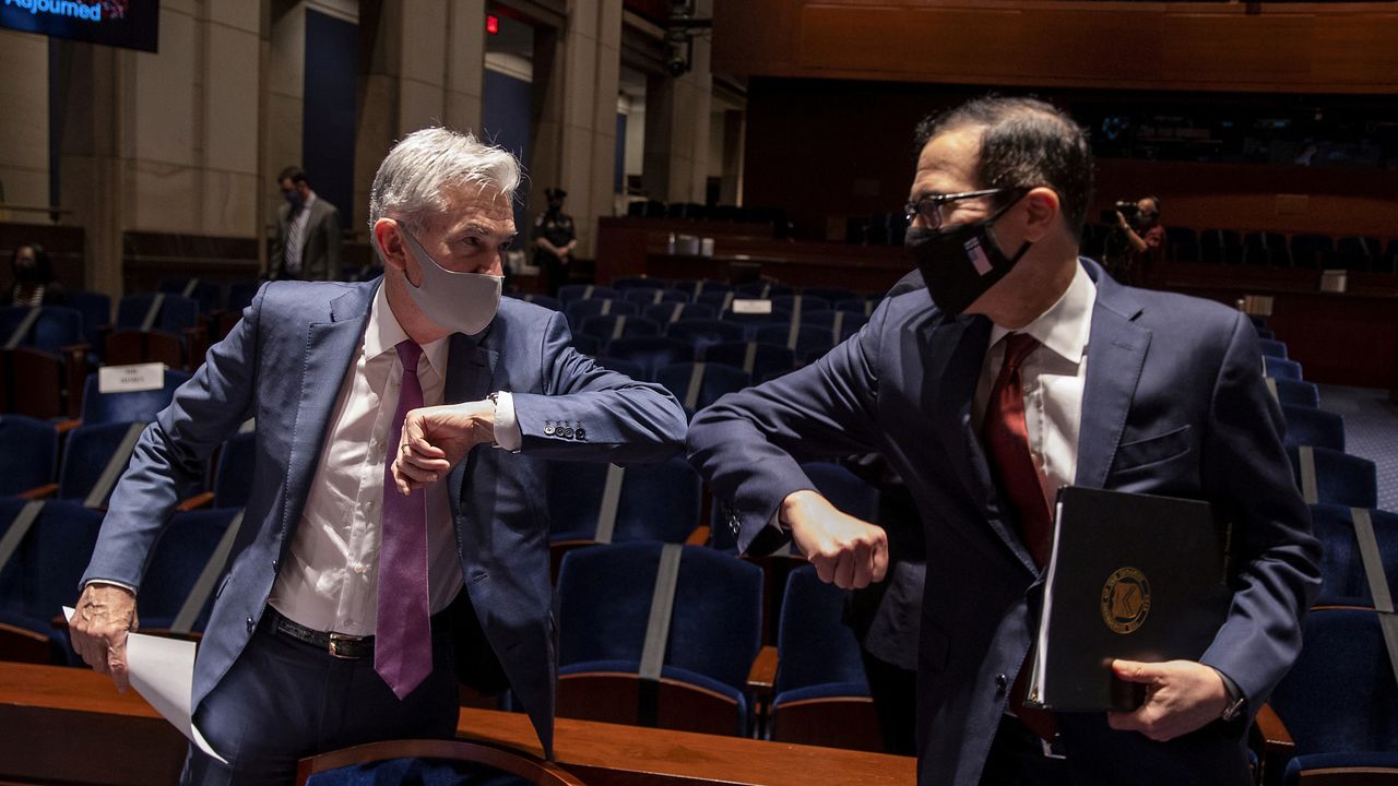 Federal Reserve Chair Jerome Powell and Treasury Secretary Steven Mnuchin elbowing each other in place of a traditional handshake during COVID pandemic.